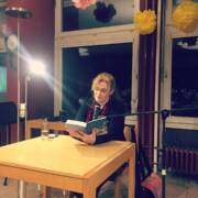 Miriam Rademacher sitzt an einem Tisch und liest aus einem Buch.