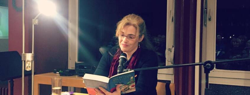 Miriam Rademacher sitzt an einem Tisch und liest aus einem Buch.